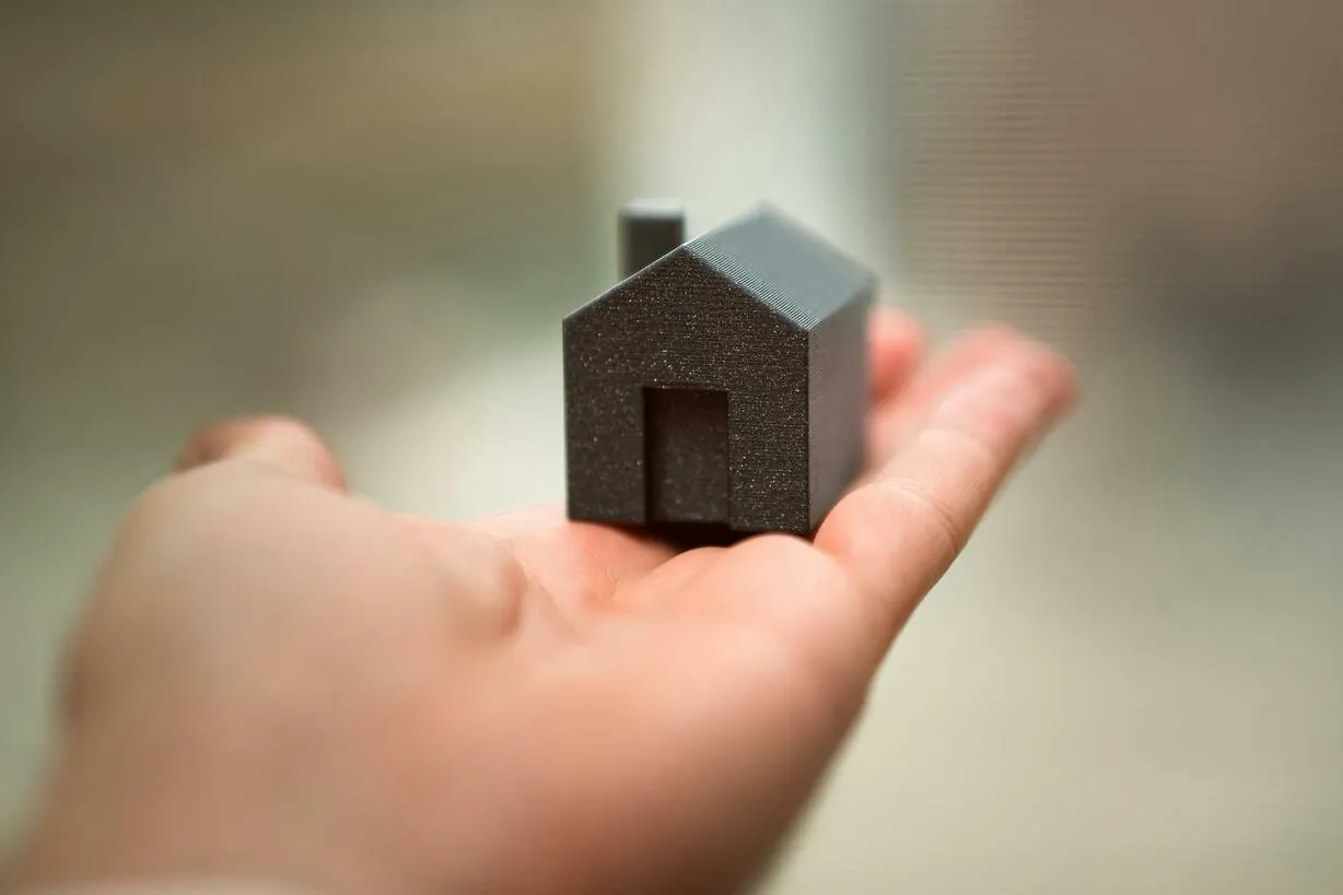 A hand holding a miniature model house, representing home buying