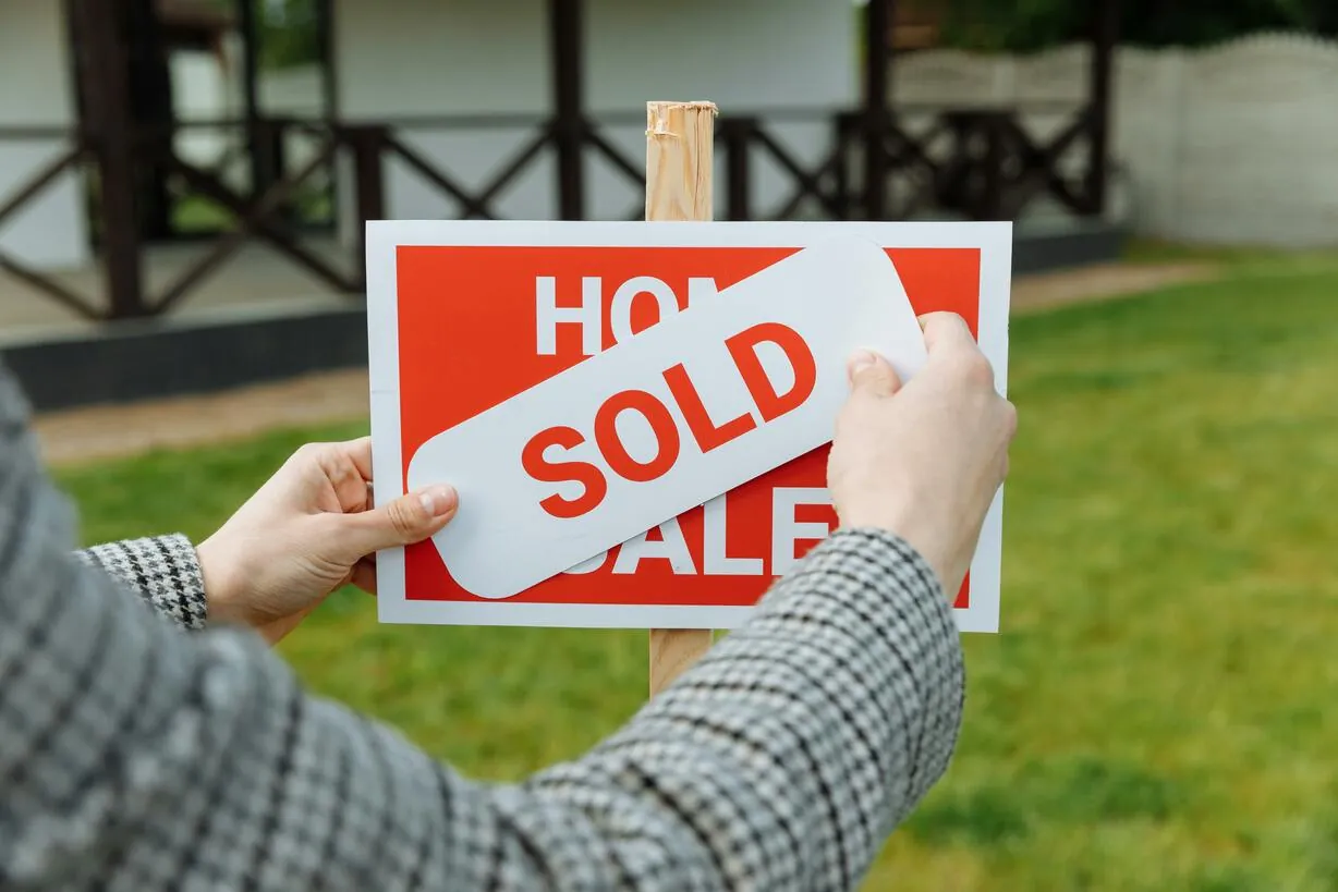 A realtor placing a "Sold" sticker on a for-sale sign